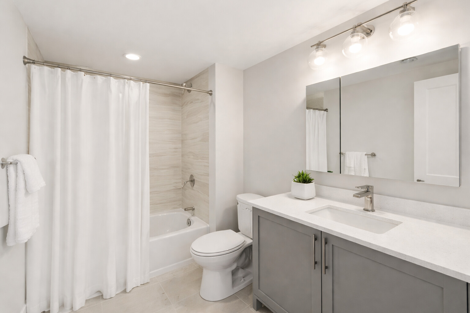 Bright, modern bathroom with gray vanity, white shower curtain, and clean finishes, located in Greater Boston