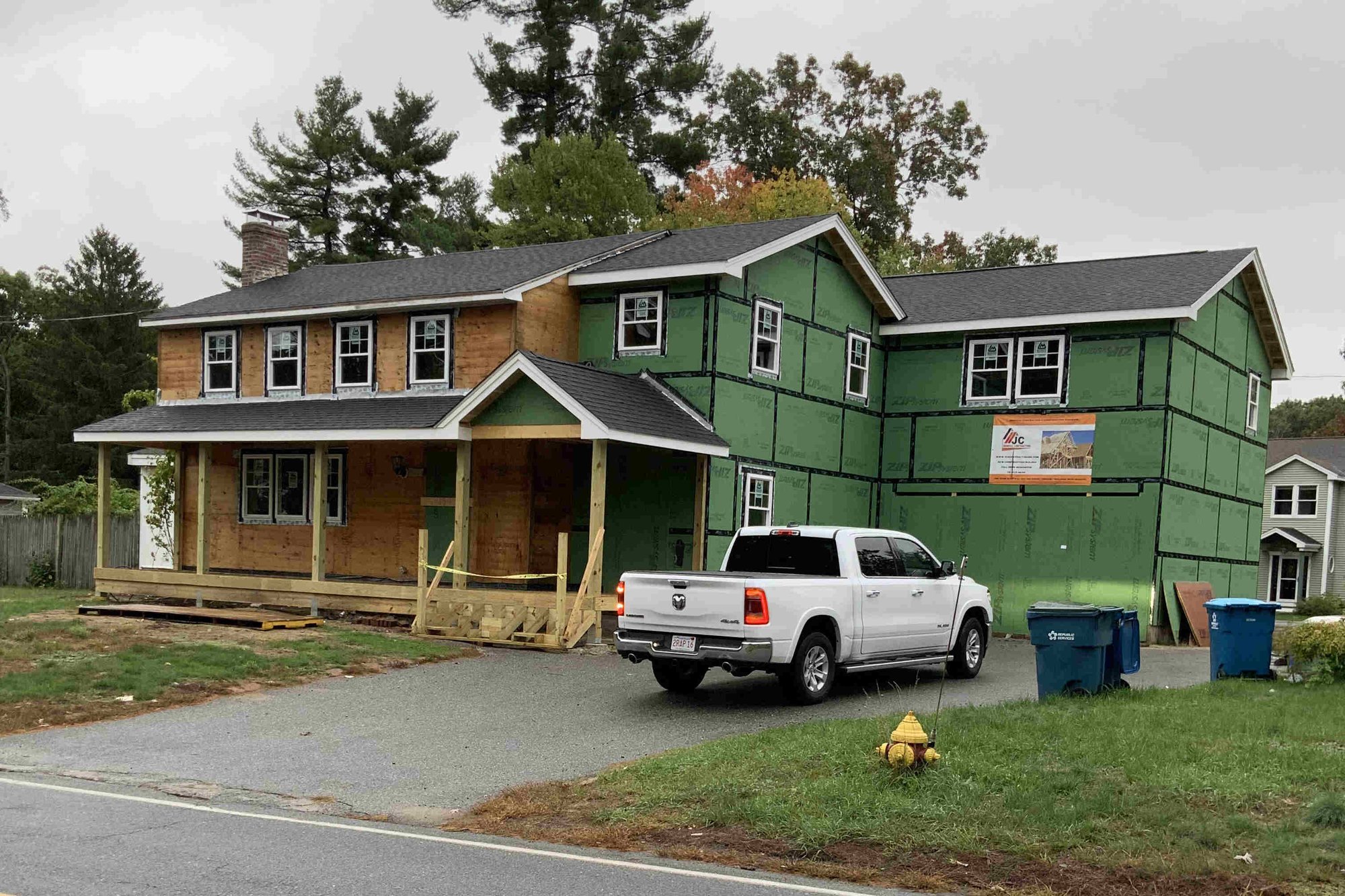 Greater Boston home under renovation with partial siding, green sheathing, front porch framing, and pickup truck in the driveway