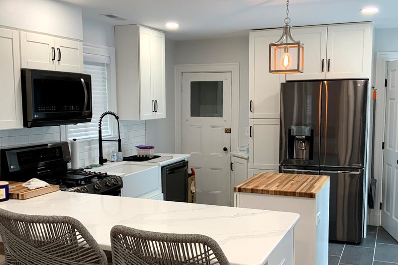 Modern white kitchen with island seating, stainless appliances, and wood-accented prep counter by Honorato Company