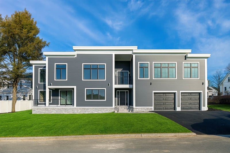 Modern gray two-story home in Boston, MA with large black-framed windows and double garage