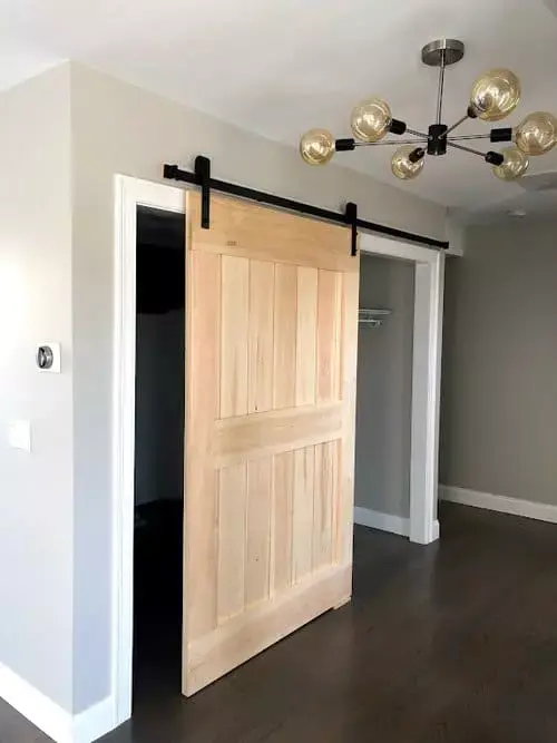 Bedroom area with natural wood sliding barn door, modern chandelier lighting, and dark hardwood floors in a contemporary home in Greater Boston