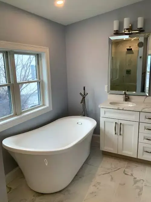 Bright bathroom with freestanding soaking tub by a window, white vanity, marble flooring, and modern fixtures in a home in Greater Boston