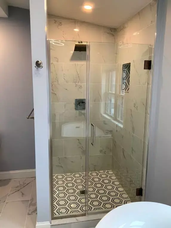 Glass walk-in shower with marble tile walls, patterned floor tile, and modern fixtures inside a renovated bathroom in Greater Boston