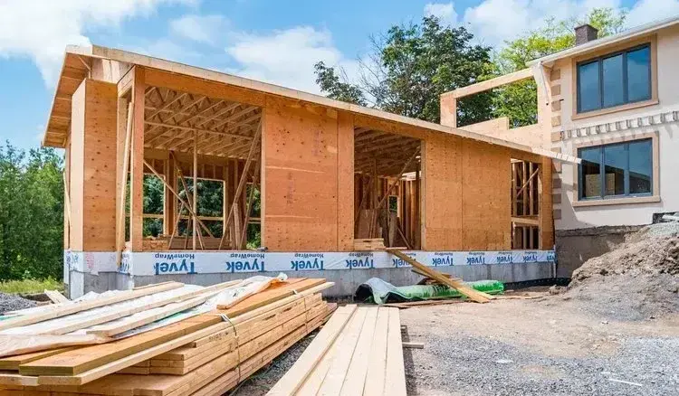 Home addition under construction with wood framing, sheathing, and stacked lumber on site, located in the Greater Boston area