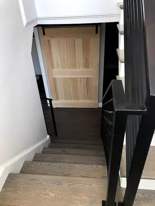 Interior staircase with dark wood railing and steps leading to a hallway with a natural wood sliding barn door in a modern home in Greater Boston