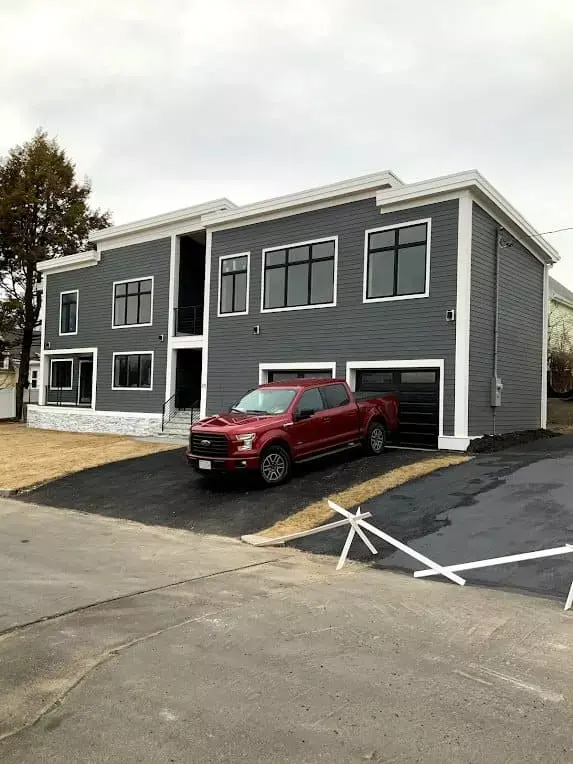 Modern gray multi-family home with black windows, garage bays, and driveway, located in the Greater Boston area Modern gray multi-family home with black windows, garage bays, and driveway, located in the Greater Boston area