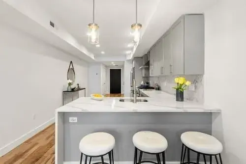 Modern kitchen with white island seating, pendant lights, gray cabinets, and hardwood floors in a contemporary condo in Greater Boston