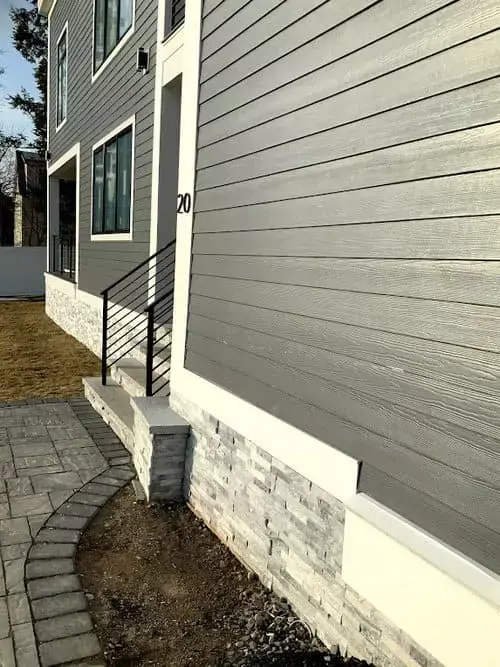 Modern townhouse exterior with gray siding, stone foundation, front steps, and paved walkway leading to the entrance in Greater Boston