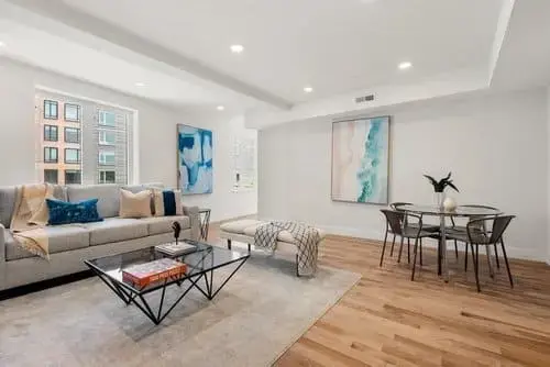 Open living and dining area with hardwood floors, sofa seating, glass coffee table, and artwork, inside a modern condo in Greater Boston
