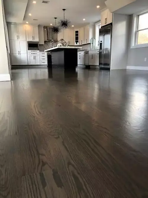 Open-concept kitchen with dark hardwood floors, large island, white cabinetry, stainless appliances, and modern lighting in a home in Greater Boston