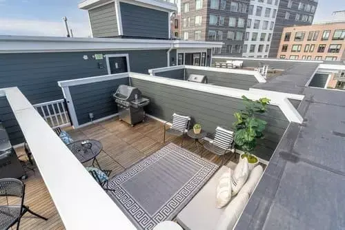 Private rooftop patio with wood decking, grill, outdoor seating, and surrounding city buildings in Greater Boston