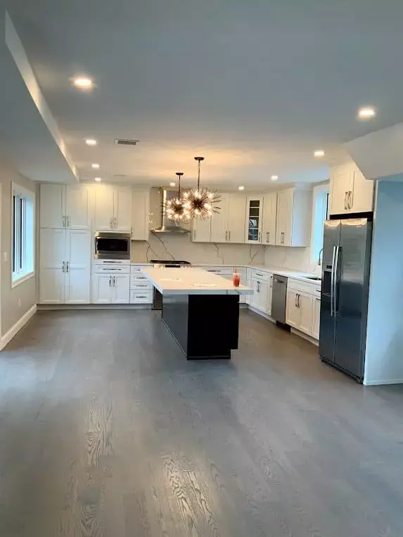 Spacious modern kitchen with white cabinets, large island, stainless steel appliances, and contemporary lighting in a home in Greater Boston.