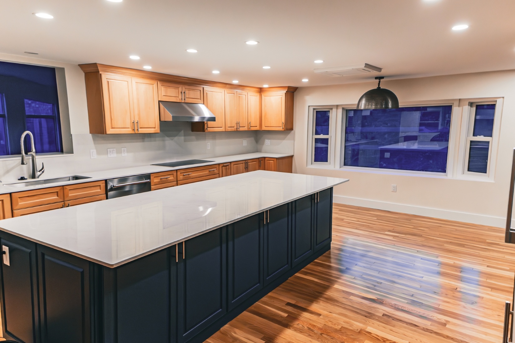Warm wood floors in kitchen with large dark island in Boston home remodel by Honorato Company