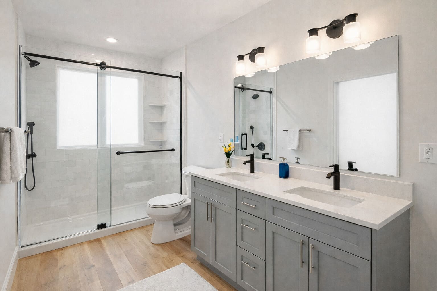 Modern bathroom with double vanity, gray cabinets, glass shower, and white tile, located in the Greater Boston area